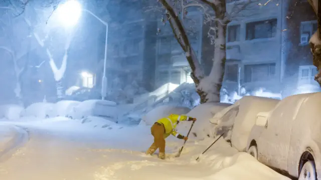 A man removes snow to drive his car as snow falls down during a winter storm in West New York, New Jersey
