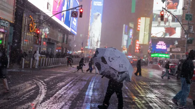 A person crossing the street in New York City holding a snow-covered umbrella during the blizzard
