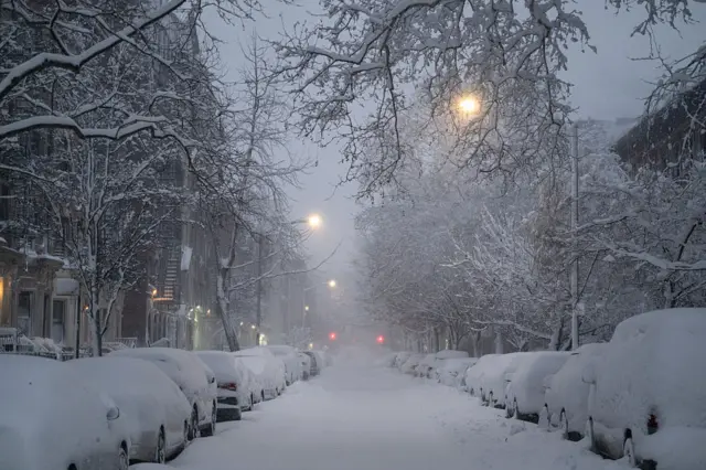 Vehicles parked along a snow-covered street during a winter storm in the Brooklyn borough of New York