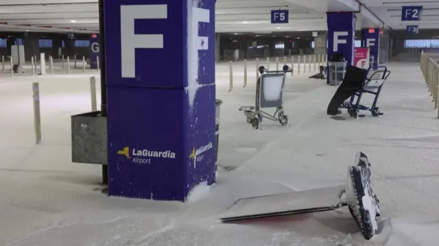Airport luggage carts sit in an empty parking lot during a winter storm at LaGuardia Airport