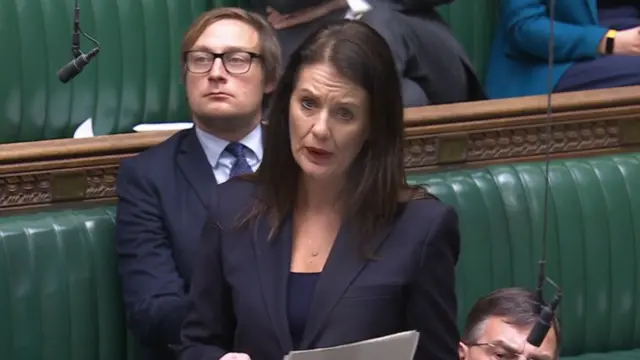 Lib Dem MP Monica Harding speaking in Commons, with other MPs behind her and holding a sheet of paper with her speech written on it