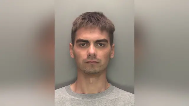 Police custody photograph of Deividas Skebas. He has short brown hair and is wearing a light grey top