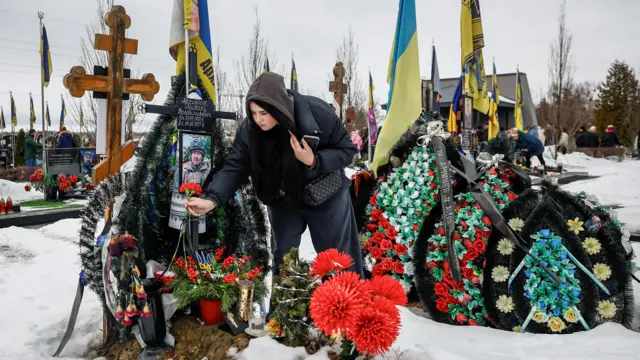 A woman leaves flowers at a memorial among lots of other floral tributes
