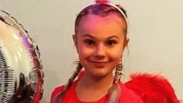 Family photograph of Lilia. She has blond hair in plaits and is wearing a read outfit