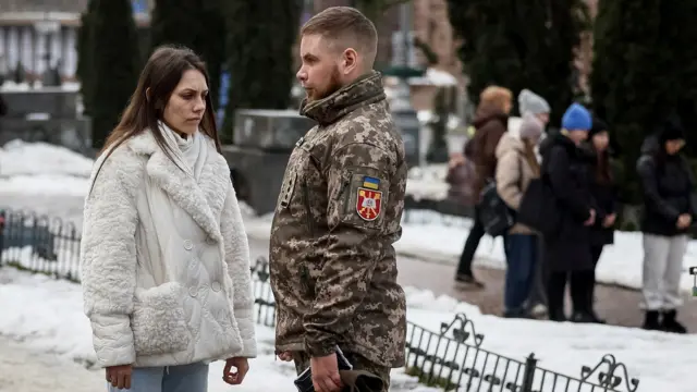 A woman in a white coat stands opposite a soldier in military uniform