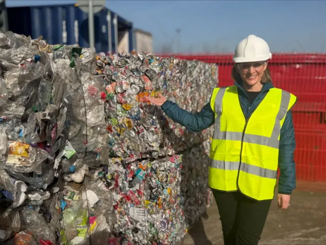 A woman in a hard hat ans high vis vest stands next to a large pile of compacted waste