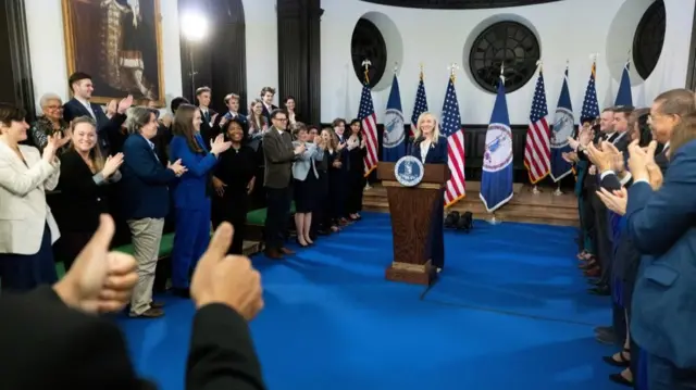 A person gives two thumbs up as others applaud Abigail Spanberger as she stands behind a lectern