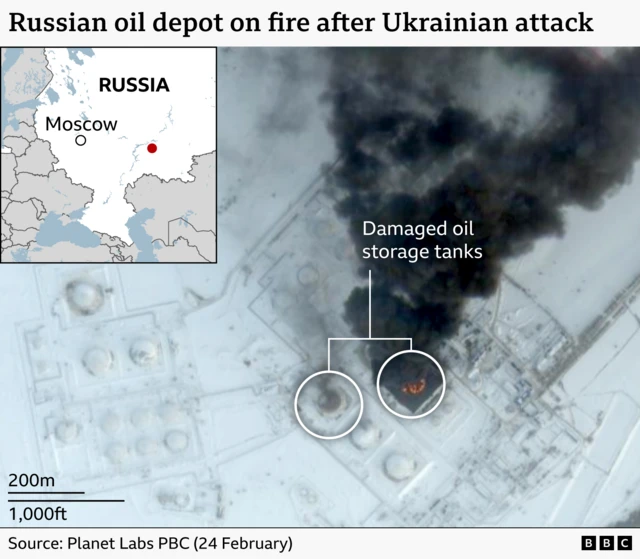 Satellite image of an oil depot with storage tanks highlighted. One has signs of damage and the other is on fire and has a huge plume of black smoke coming from it.