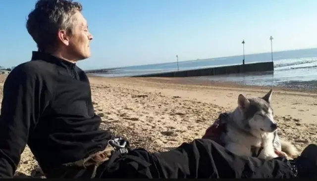 A man and a dog siting on a beach looking out to sea