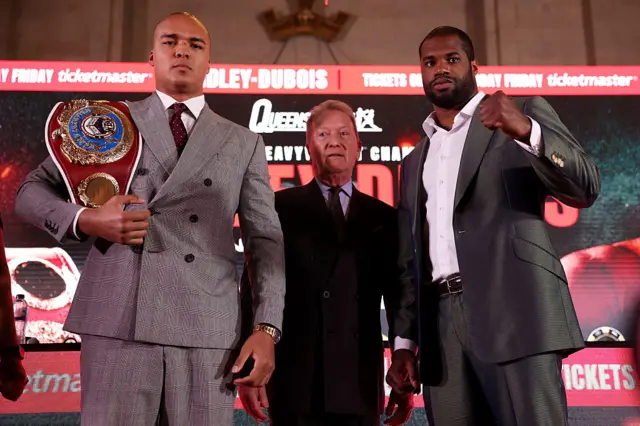 Fabio Wardley holds up his fist and has the WBO title on his shoulder and is standing next to Daniel Dubois and Frank Warren