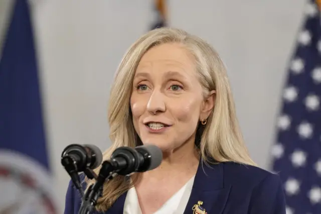A blonde woman speaks into two microphones