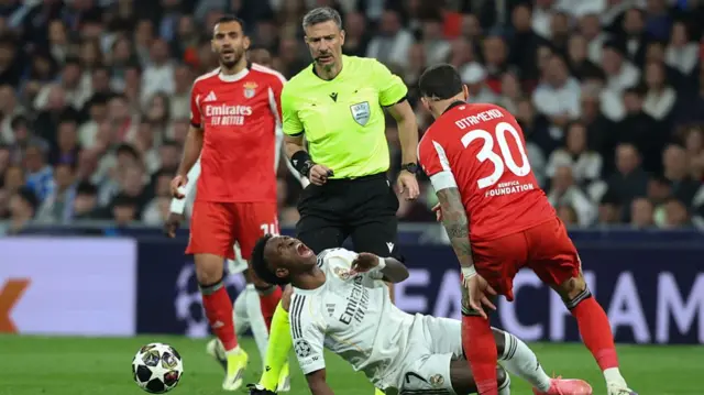 Vinicius Jr goes down under a challenge by Nicolas Otamendi as the referee watches on