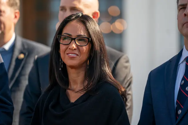 Lauren Boebert dressed in black with black rimmed glasses flanked by three men in suits
