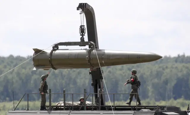 A large missile being hoisted into the air with three men standing under it