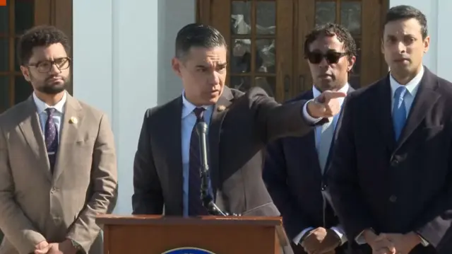 Robert Garcia speaking into microphone with other Democrats standing behind him