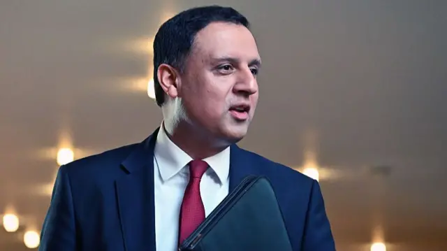 Anas Sarwar in a suit holding a black folder.