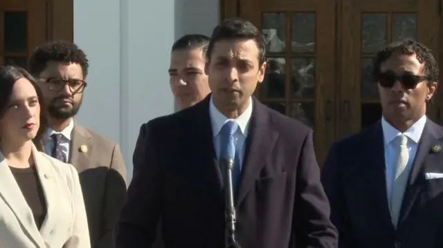Suhas Subramanyam speaking into a microphone with other Democrats behind him