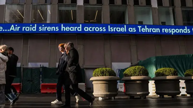 People walk by the Fox News ticker on February 28, 2026 in New York, New York. The display read Air raid sirens heard across Israel as Tehran responds