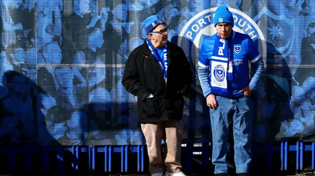 Two Portsmouth fans pictured resting against a wall outside Fratton Park