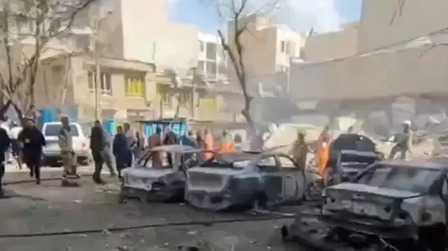 People gather near a row of burnt vehicles in Tehran, Iran