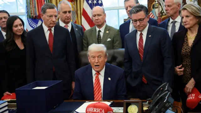 अमेरिकी राष्ट्रपति डोनाल्ड ट्रम्प अपनी मेज पर बैठे हैं, एक टोपी के पीछे जिस पर लिखा है "अमेरिका वापस आ गया है", जबकि यूएस हाउस के अध्यक्ष माइक जॉनसन (आर-एलए), सीनेटर शेली मूर कैपिटो (आर-डब्ल्यूवी) और सीनेटर जॉन बैरासो (आर-डब्ल्यूवाई) वाशिंगटन, डीसी, यूएस में व्हाइट हाउस में 3 फरवरी, 2026 को उनके साथ खड़े थे।