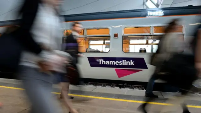 People, blurred, walking past a Thameslink train.
