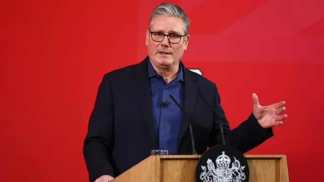 Starmer talking at a pedestal in front of a red background