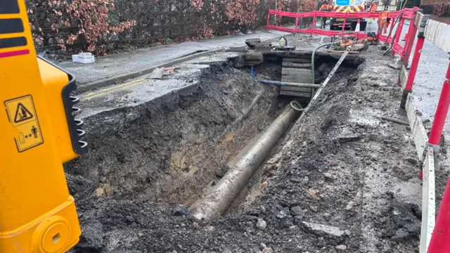 A large hole in the road at the scene of a burst water main. The pipe can be seen.