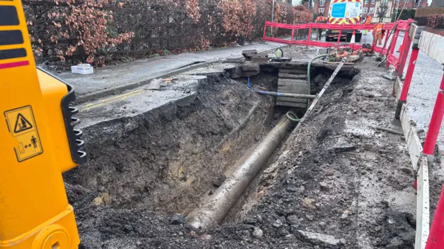 An exposed water pipe in the ground surrounding my machinery, fencing and cones on the street