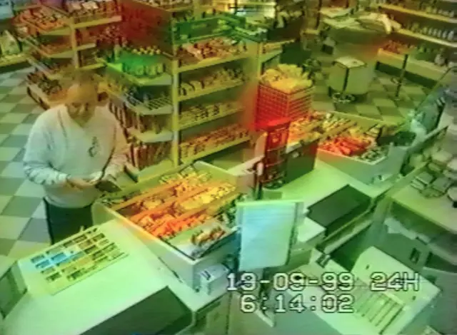 A CCTV image of Steve Wright at a petrol station counter. He wears a grey jumper and trousers. He holds a wallet in his hands.
