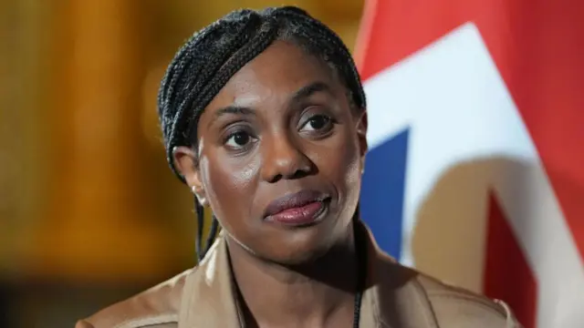 Tory leader Kemi Badenoch standing in front of a red, blue and white sign