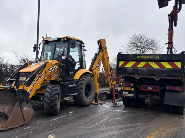 A yellow JCB digger at the scene of a burst water main