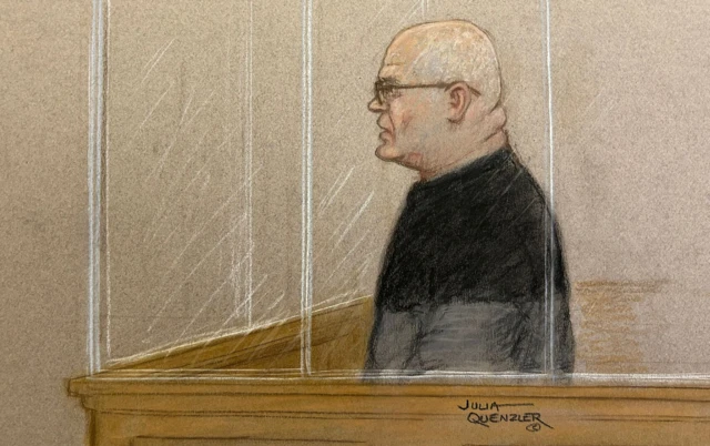 An artist's impression of Steve Wright in a court room dock. He sits in the booth wearing glasses and a black top, there is a signature on the bottom right hand side of the image that says 'Julia Quenzler'.