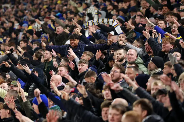Leeds fans chant and raise their arms in the air