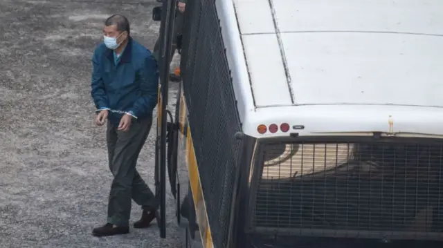 Jimmy Lai walks out of a bus with handcuffs