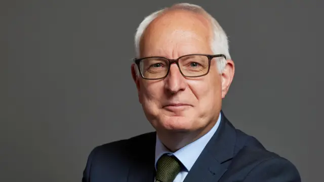 Official parliamentary portrait photo of Neil Duncan-Jordan. He has white hair and is wearing black-rimmed glasses, a navy blue suit, with a light blue shirt and moss gre
