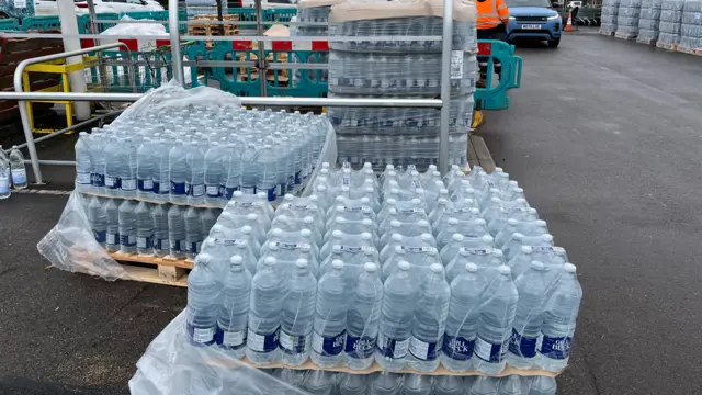 Crates and trollies full of bottled water at a supermarket car park.