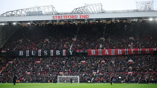 A banner reading 'Busby Babes' drops down from the Stretford End