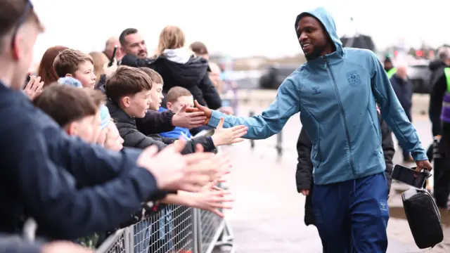 Frank Onyeka (right) wears a Coventry jacket with the hood over his head as he holds his hand out to clap hands with fans waiting behiind a barrier