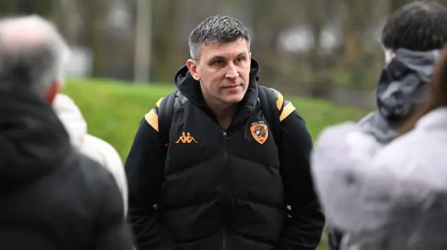 Sergej Jakirovic standing with his hands in his pockets as fans look at him as Hull get off the team bus