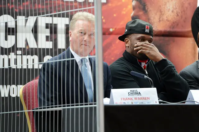 Frank Warren sits next to Derek Chisora and they are behind a fence
