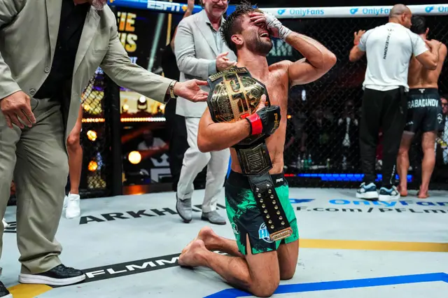 Alfie Davis is on his knees and has his hand over his face as he holds the PFL lightweight tournament belt over his shoulder