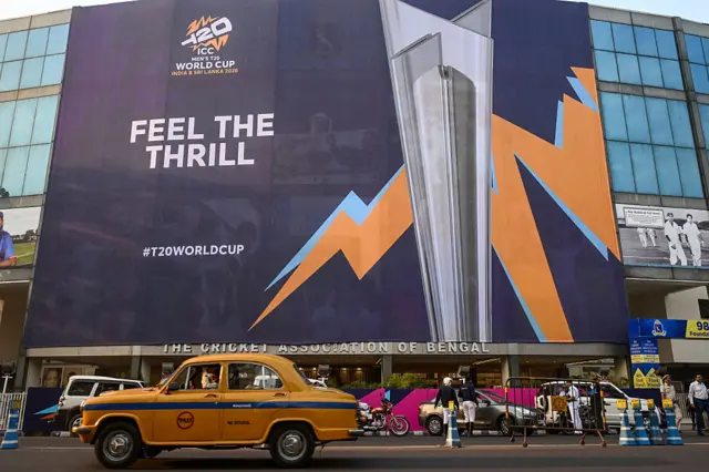 A taxi driver rides past a billboard featuring the 2026 ICC Men's T20 Cricket World Cup trophy, displayed outside the Eden Gardens in Kolkata