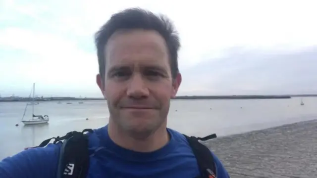A man in a blue T shirt. He has a black backpack on.