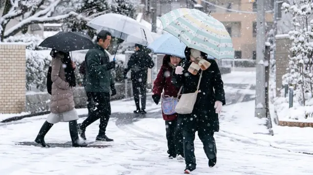 people holding umbrellas as they walk in the snow
