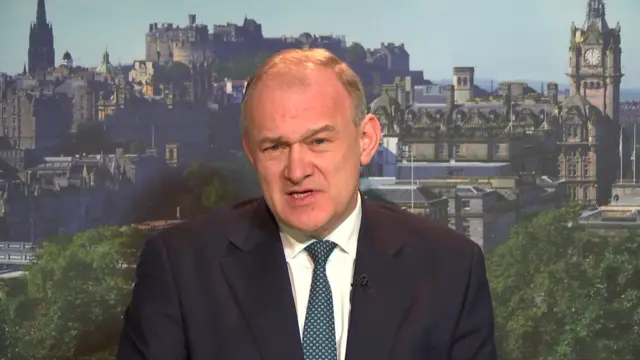 Ed Davey speaks to camera in front of an artificial background showing an image of Edinburgh