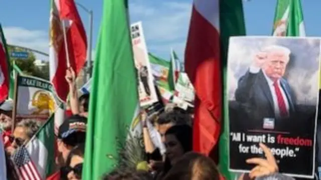 A crowd waves flags while one person holds a poster of US Donald Trump with the quote: "All I want is freedom for the people"