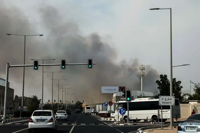 Motorists drive past a plume of smoke rising from a reported Iranian strike in the industrial district of Doha