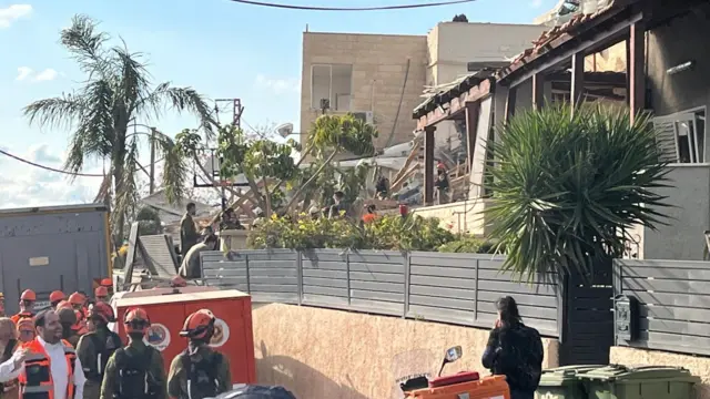 Emergency respondents on the left side of the image observe the remains of a building heavily damaged in a missile strike