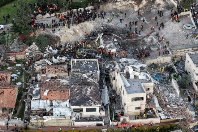 Drone footage of emergency response in Beit Shemesh following a strike. Several buildings appear heavily damaged, with one property at the cent